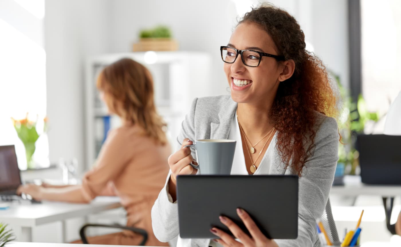 Lachende medewerker met koffie en tablet op kantoor