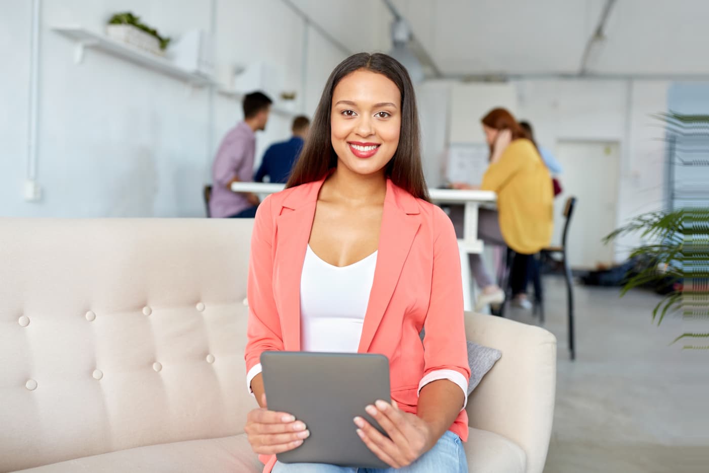 Medewerker met tablet op een bank in een open kantoor